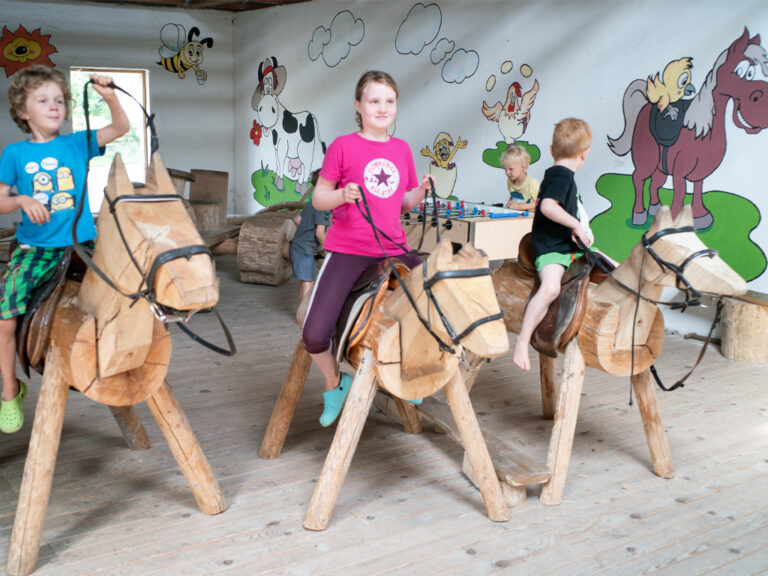 kinder reiten auf holzpferden im indoorspielplatz des ferienbauernhof ohr